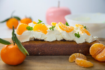 Vegan tangerine sponge cake with a giant frosting and mandarin orange wedges on a wooden board.