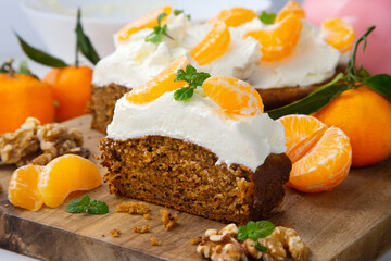 Vegan tangerine sponge cake with a giant frosting and mandarin orange wedges on a wooden board.