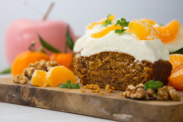 Vegan tangerine sponge cake with a giant frosting and mandarin orange wedges on a wooden board.