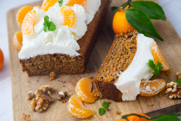 Vegan tangerine sponge cake with a giant frosting and mandarin orange wedges on a wooden board.