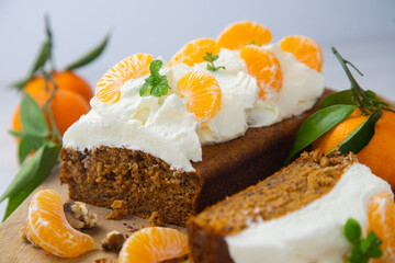 Vegan tangerine sponge cake with a giant frosting and mandarin orange wedges on a wooden board.