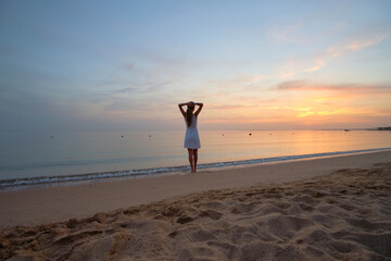 Lonely young woman standing on sandy beach by seaside enjoying warm tropical evening