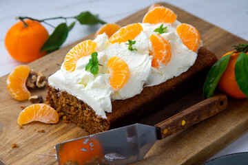 Vegan tangerine sponge cake with a giant frosting and mandarin orange wedges on a wooden board.