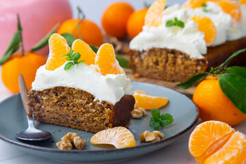 Vegan tangerine sponge cake with a giant frosting and mandarin orange wedges on a wooden board.