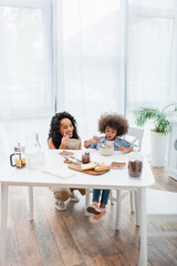 Smiling african american family eating breakfast near milk and tea in kitchen.