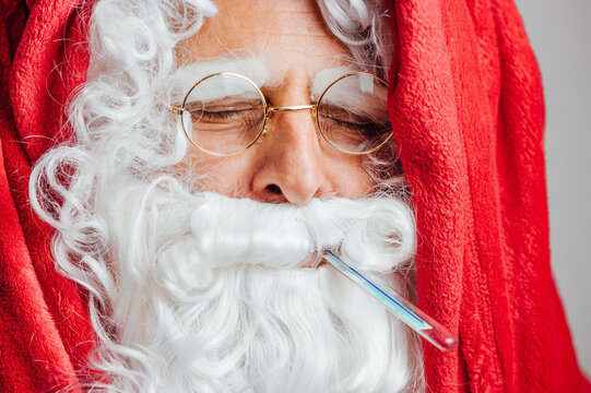 Santa sick with cold wrapped in blanket and with thermometer in mouth