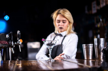 Young girl mixologist formulates a cocktail while standing near the bar counter in nightclub