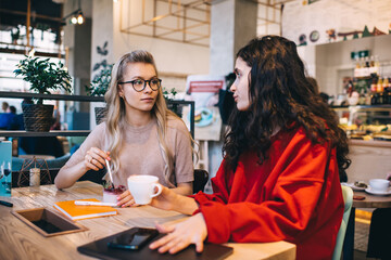 Young women with devices sitting in cafe during break