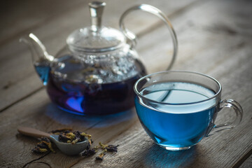 Obraz na płótnie Canvas Butterfly pea blue tea in a glass cup on a wooden table, a teapot and dry leaves of clitoria trifoli