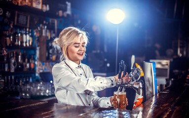 Charismatic girl bartender pouring fresh alcoholic drink into the glasses while standing near the bar counter in nightclub