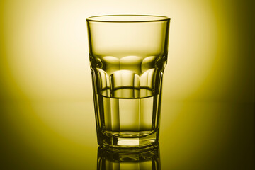 Half-filled highball glass in yellow light with mirror reflection. Close-up.