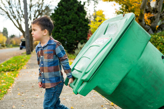 Boy pulling yard waste bin to sidewalk on street