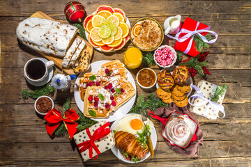 Festive Christmas morning breakfast or brunch table, with traditional foods – pancakes, Belgian waffles, fried eggs, croissant, stolen, cookies, with orange juice and coffee, cinnamon rice porridge 