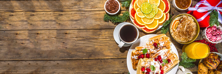 Festive Christmas morning breakfast or brunch table, with traditional foods – pancakes, Belgian waffles, fried eggs, croissant, stolen, cookies, with orange juice and coffee, cinnamon rice porridge 