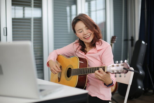 Young women musician is online training lesson classes playing guitar at home and play music.