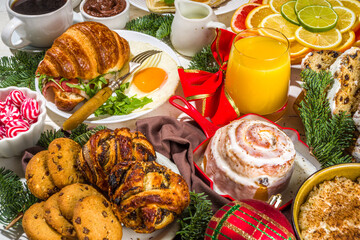 Festive Christmas morning breakfast or brunch table, with traditional foods – pancakes, Belgian waffles, fried eggs, croissant, stolen, cookies, with orange juice and coffee, cinnamon rice porridge 