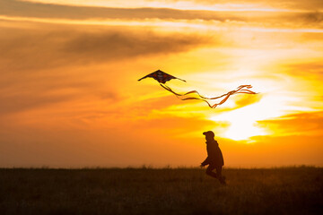 Flying a kite. The boy runs across the field with a kite. Silhouette of a child against the sky. Bright sunset. - Powered by Adobe