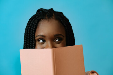 portrait of a beautiful young african american woman with a book on a blue background