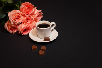 Cup of coffee, heart shape chocolate candies and pink roses.