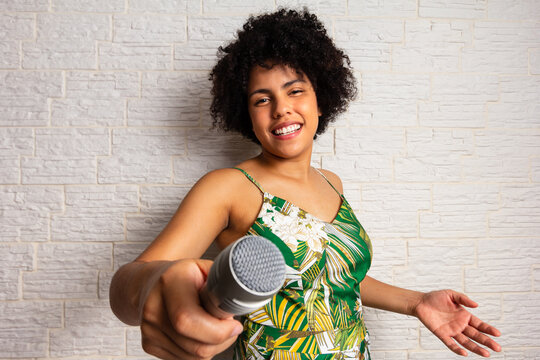 Lovely brazilian woman with curly afro hair playing karaoke and holding microphone, passsing the turn, inviting, calling more to sing along. Speak up. 