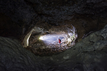 spéléologue dans une entrée de grotte avec un trou de lumière - obrazy, fototapety, plakaty
