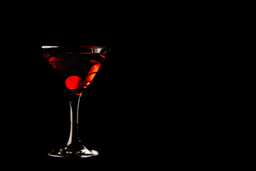 martini glass with red cocktail with cherry on black background