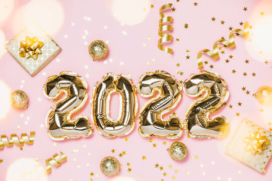 New year 2022 balloon celebration card. Gold foil balloon number 2022, party decoration, gold confetti on pink background. Flat lay, merry christmas, happy holidays concept.