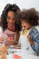Happy african american kid standing near mom cooking in kitchen.