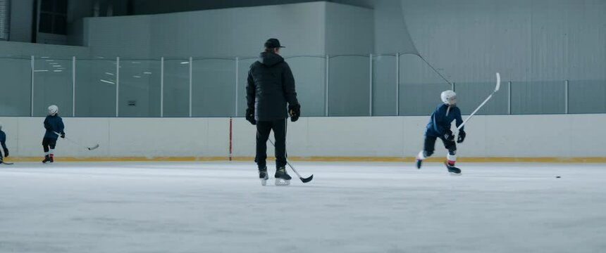 Coach is watching the kids ice hockey practice inside indoor rink. Shot with 2x anamorphic lens