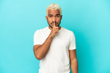 Young Colombian handsome man isolated on blue background showing a sign of silence gesture putting finger in mouth