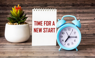 TIME FOR A NEW START text on notepad and wooden background with clock and cactus flower.
