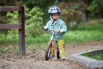 Child on a running balance bike on an autumn or summer cold day. Mittens on the hands