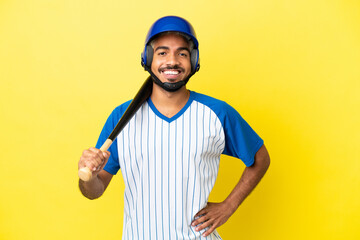 Young Colombian latin man playing baseball isolated on yellow background posing with arms at hip and smiling
