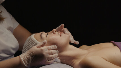 Obraz na płótnie Canvas Woman receiving facial massage in spa salon on massage table. Wellness body and skin care, face beauty treatment, receiving rejuvenation procedure