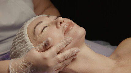 Woman receiving facial massage in spa salon on massage table. Wellness body and skin care, face beauty treatment, receiving rejuvenation procedure