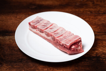 Fresh raw meat and pork ribs on a white plate on a wooden background.