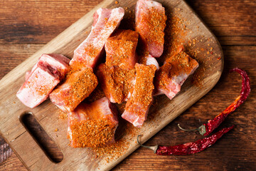 Raw pork ribs sprinkled with hot pepper. On a wooden background. Preparing for a barbecue.