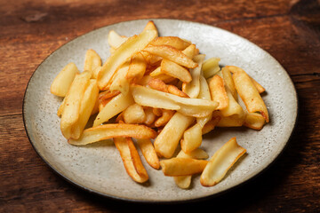 Fried French fries in wedges on a plate on a wooden background.