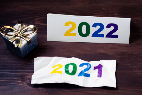 2022 numbers and crumpled 2021 of the outgoing year and new year gift on wooden background.