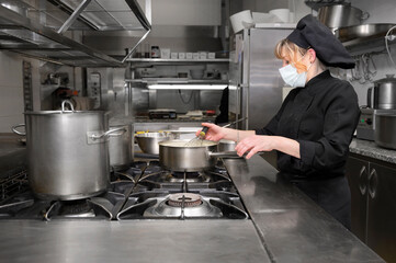 Female chef cooking in the kitchen at restaurant wearing protective medical mask in coronavirus new normal concept. High quality photo