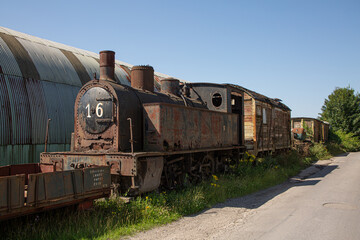 Rusty old steam train parked on grass in front of small warehouse