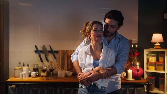 Man and woman dancing in cozy kitchen, romantic date dinner. Young husband and wife hugging in evening. Loving couple, happy marriage, family relationships. Celebrating Valentine's Day together. 