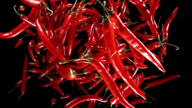 Super slow motion of flying red hot chilli peppers isolated on black background. Overhead view, filmed on high speed cinema camera, 1000 fps. Ultimate perspective of flying food. Speed ramp effect.