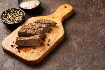 A piece of cooked beef meat steak on wooden board cut in slices, white and black peer, coarse sea salt