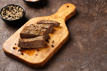 A piece of cooked beef meat steak on wooden board cut in slices, white and black peer, coarse sea salt