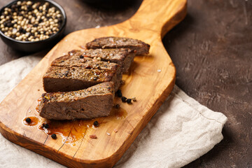 A piece of cooked beef meat steak on wooden board cut in slices, white and black peer, coarse sea salt