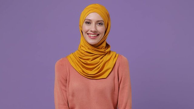 Smiling young arabian asian muslim woman in abaya hijab yellow clothes look camera isolated on plain pastel light violet background studio portrait. People uae middle eastern islam religious concept