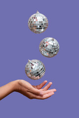 disco ball floating in the air under hand against light purple background 
