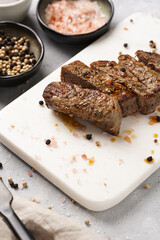 A piece of cooked beef meat steak on white marble board cut in slices, white and black peer, coarse sea salt