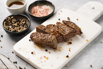 A piece of cooked beef meat steak on white marble board cut in slices, white and black peer, coarse sea salt